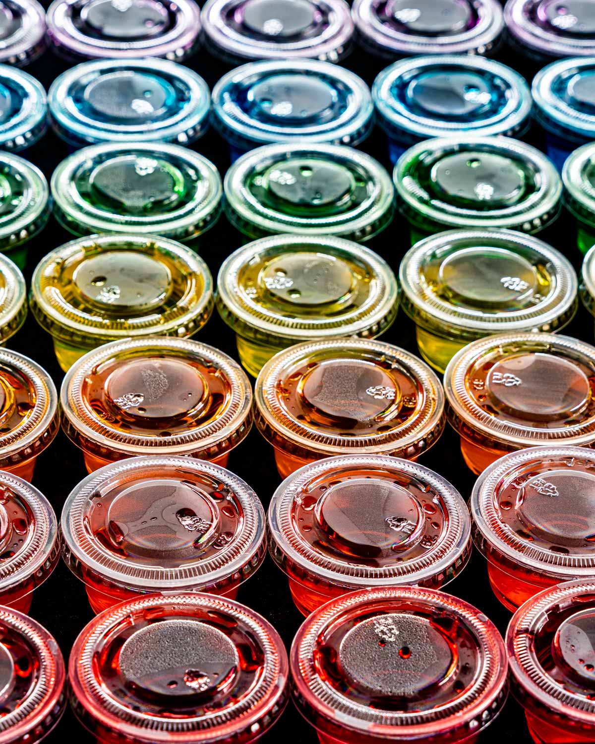 sideview shot of a rainbow of jello shots in little plastic cups with lids on