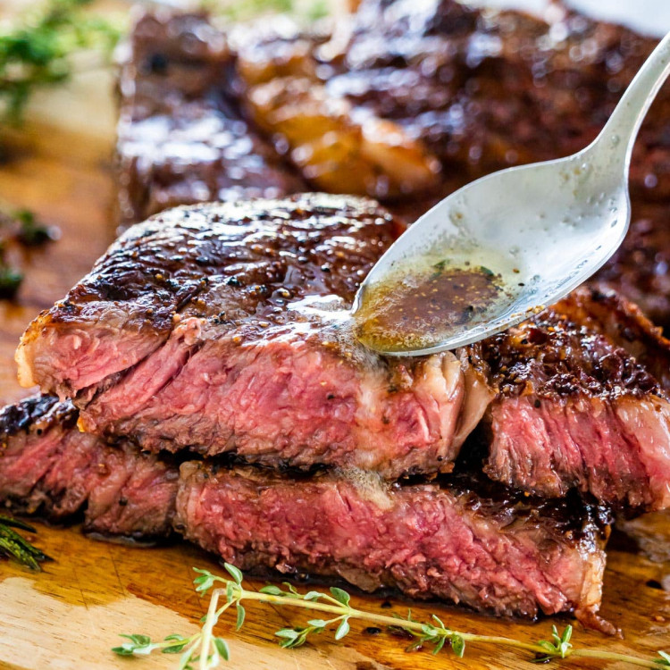 a ribeye steak cut in half and stacked with a spoon drizzling some browned butter over it