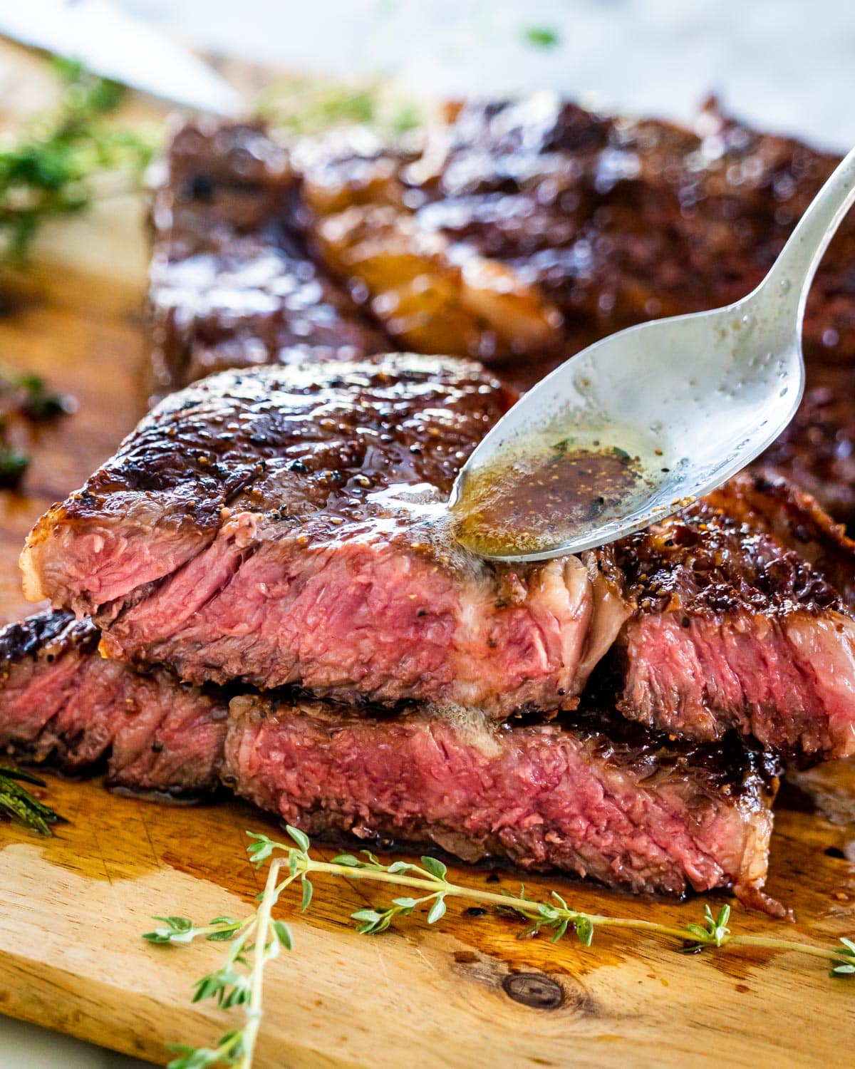 a ribeye steak cut in half and stacked with a spoon drizzling some browned butter over it
