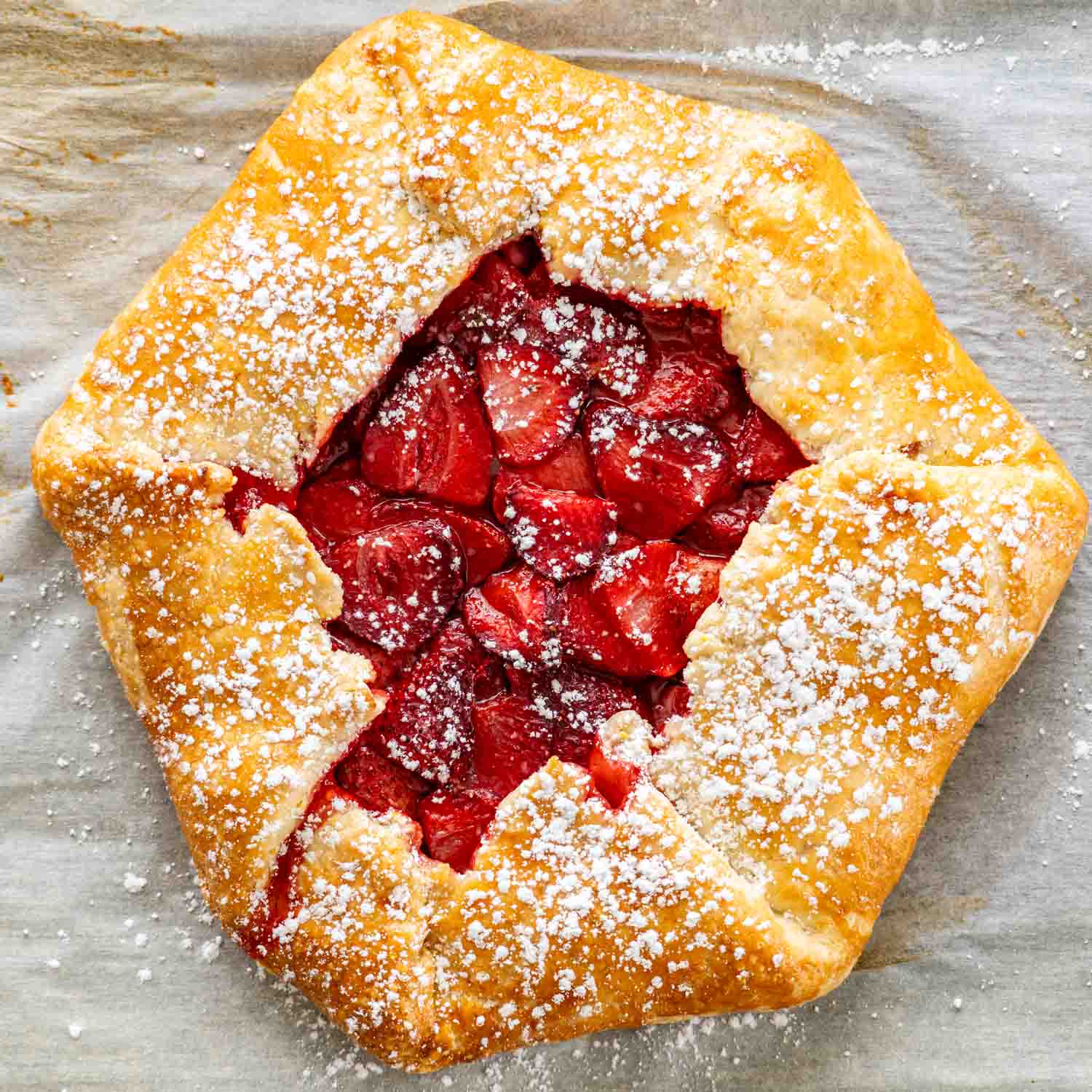 a beautiful strawberry galette on a baking sheet lined with parchment paper and sprinkled with powdered sugar.