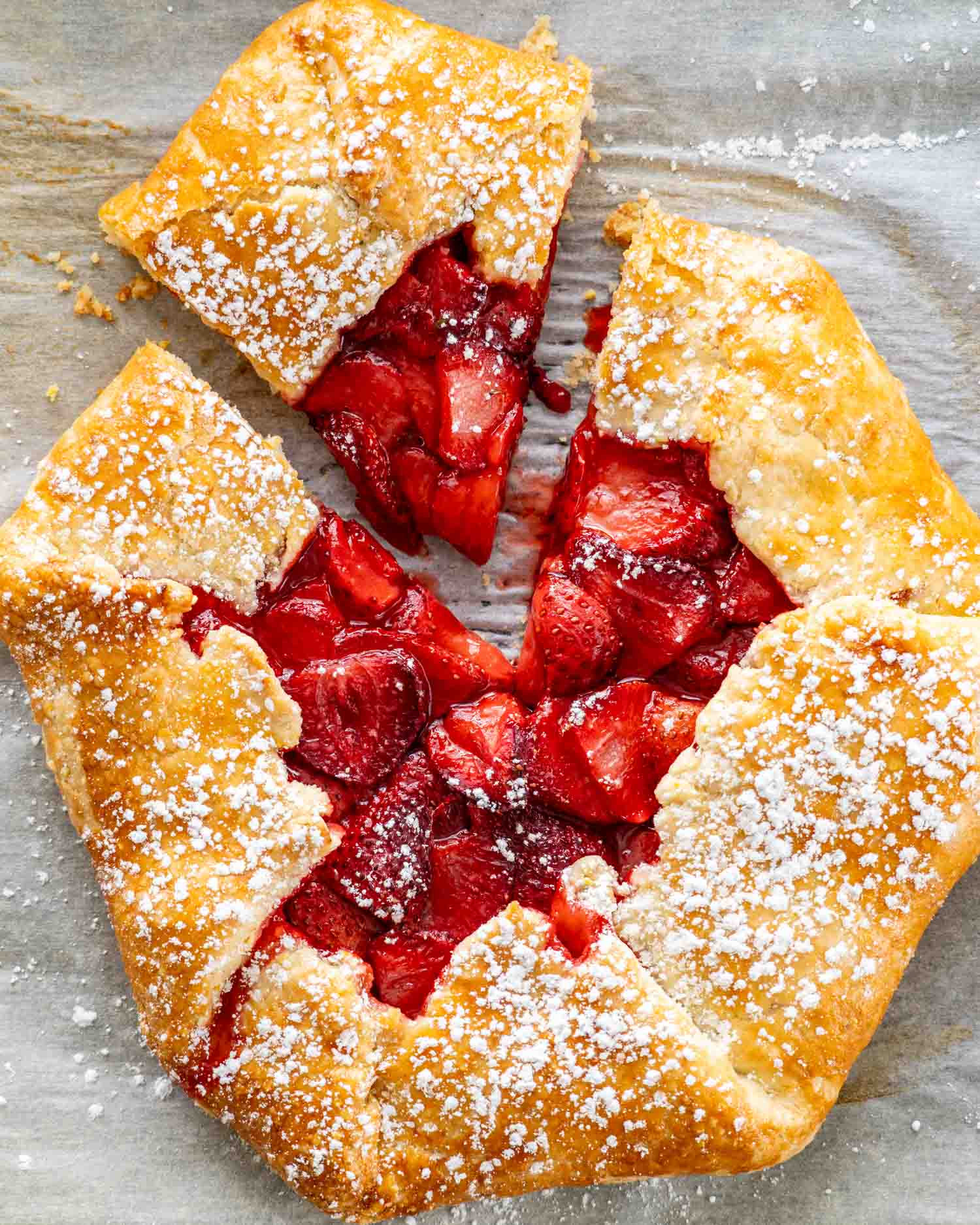 overhead shot of a strawberry galette on parchment paper sprinkled with some powdered sugar and a piece cut out of it.