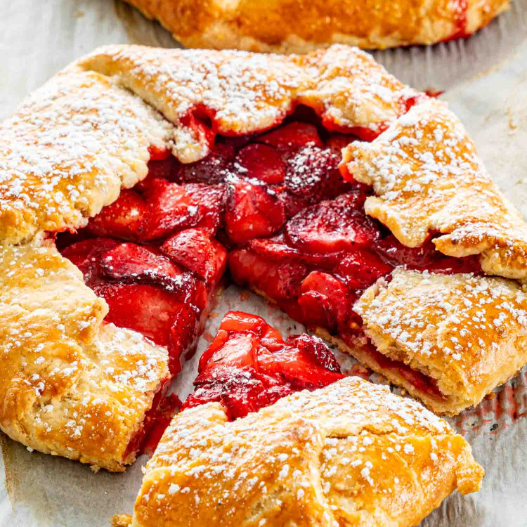 side view shot of a strawberry galette on parchment paper sprinkled with some powdered sugar and a piece cut out of it.