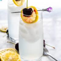 two glasses with tom collins garnished with lemon wheel and cherry