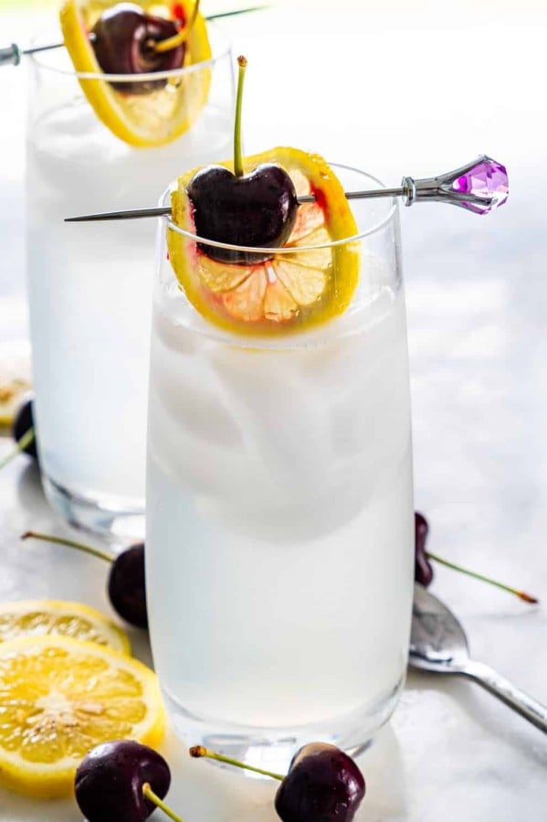 two glasses with tom collins garnished with lemon wheel and cherry