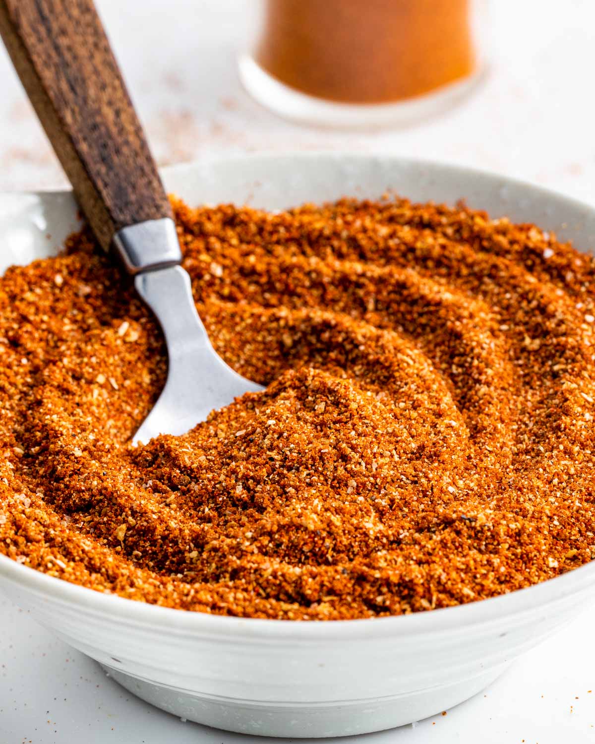 a white bowl full of bbq dry rub with a tablespoon in it