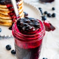side view shot of blueberry sauce in a jar with a ladle picking some up