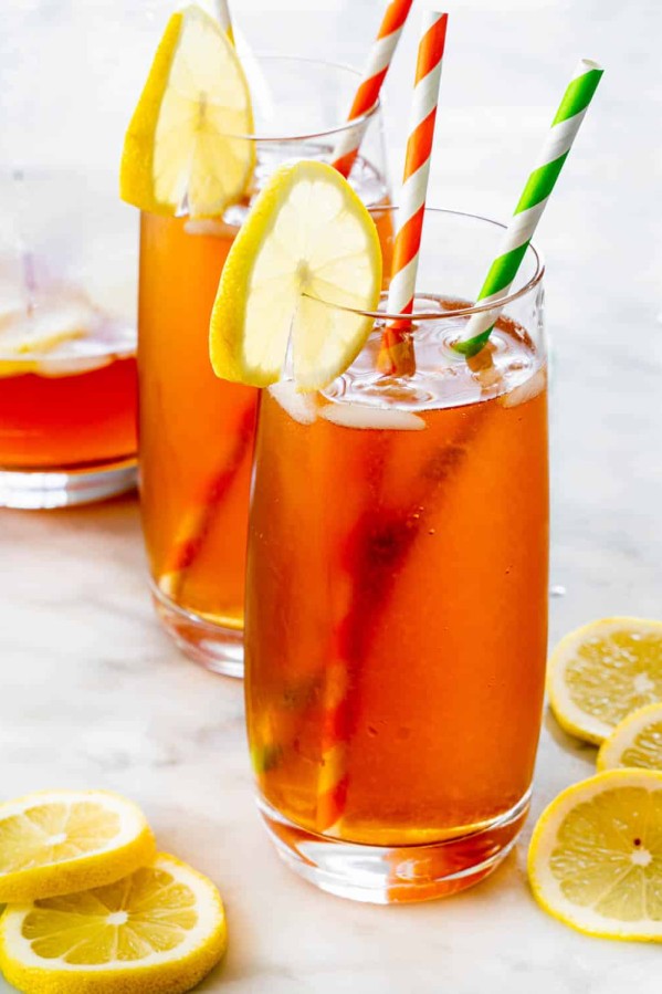 two glasses with boozy palmer arnold drink each with two straws in and lemon slice