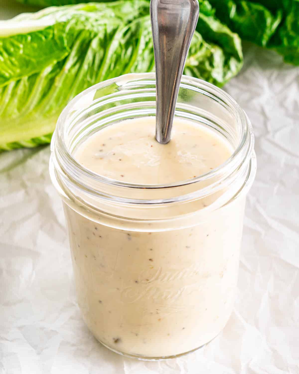 a jar with caesar salad dressing and a spoon inside