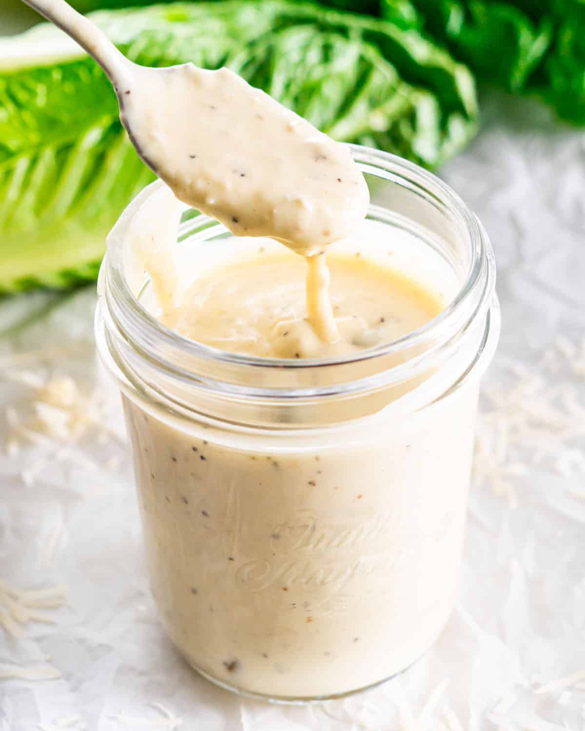 a spoon spooning some dressing from a jar full of caesar dressing