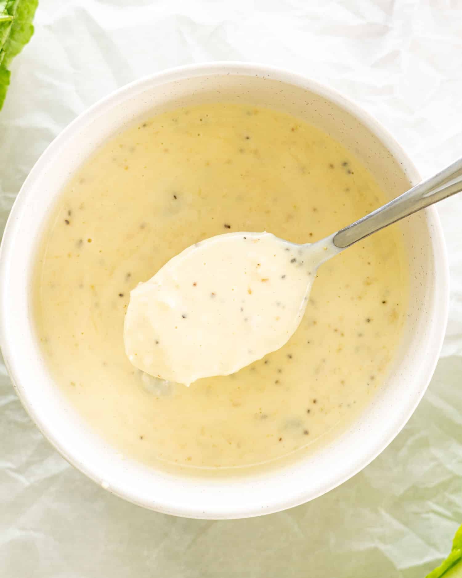 freshly made caesar salad dressing in a bowl with a teaspoon inside.