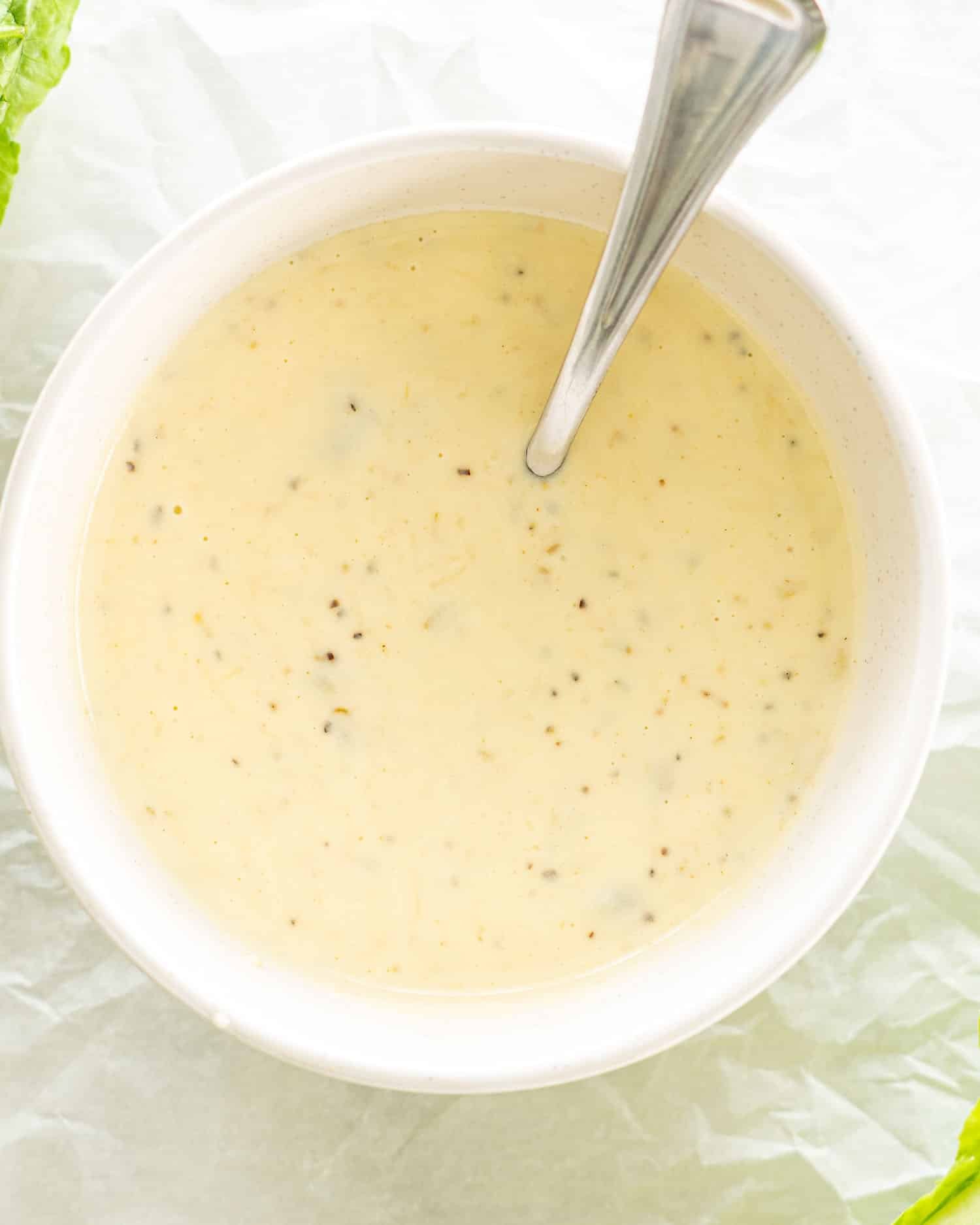 freshly made caesar salad dressing in a bowl with a teaspoon inside.