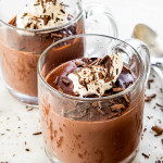 side view shot of two cups of homemade chocolate pudding topped with whipped cream and chocolate shavings