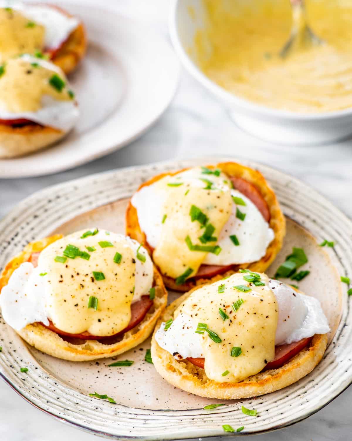3 eggs benedict on a large plate garnished with chives
