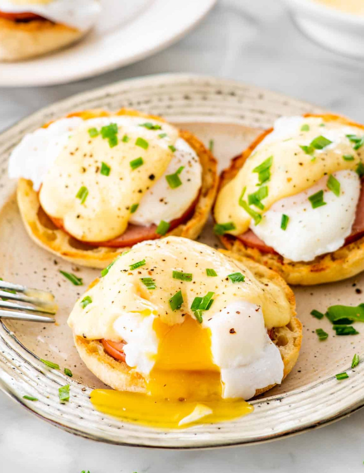 3 eggs benedict on a large plate garnished with chives