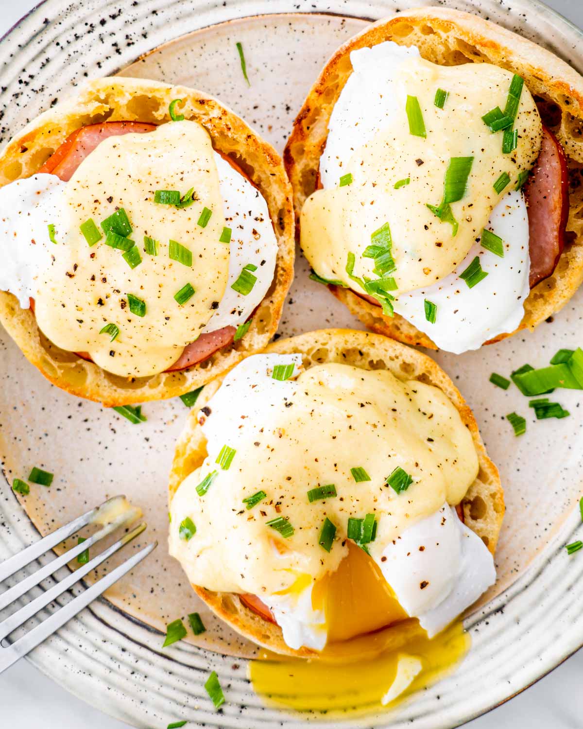 3 eggs benedict on a large plate garnished with chives