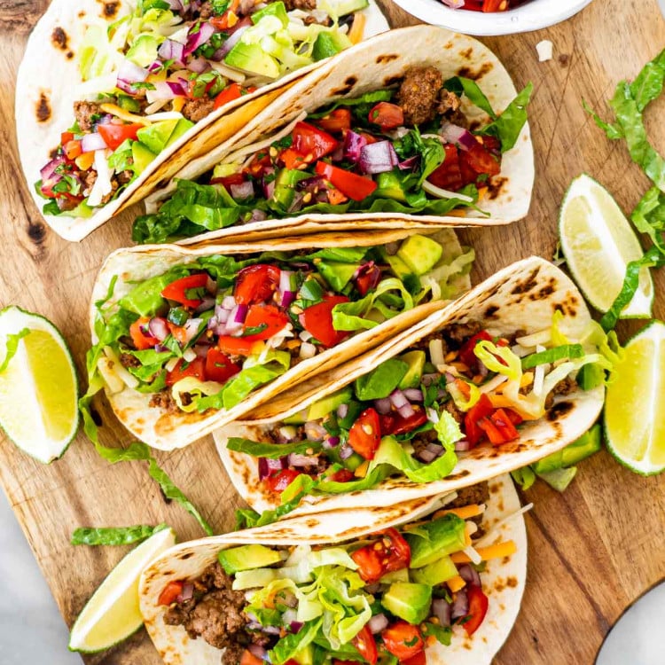 overhead shot of ground beef tacos topped with pico de gallo on a cutting board