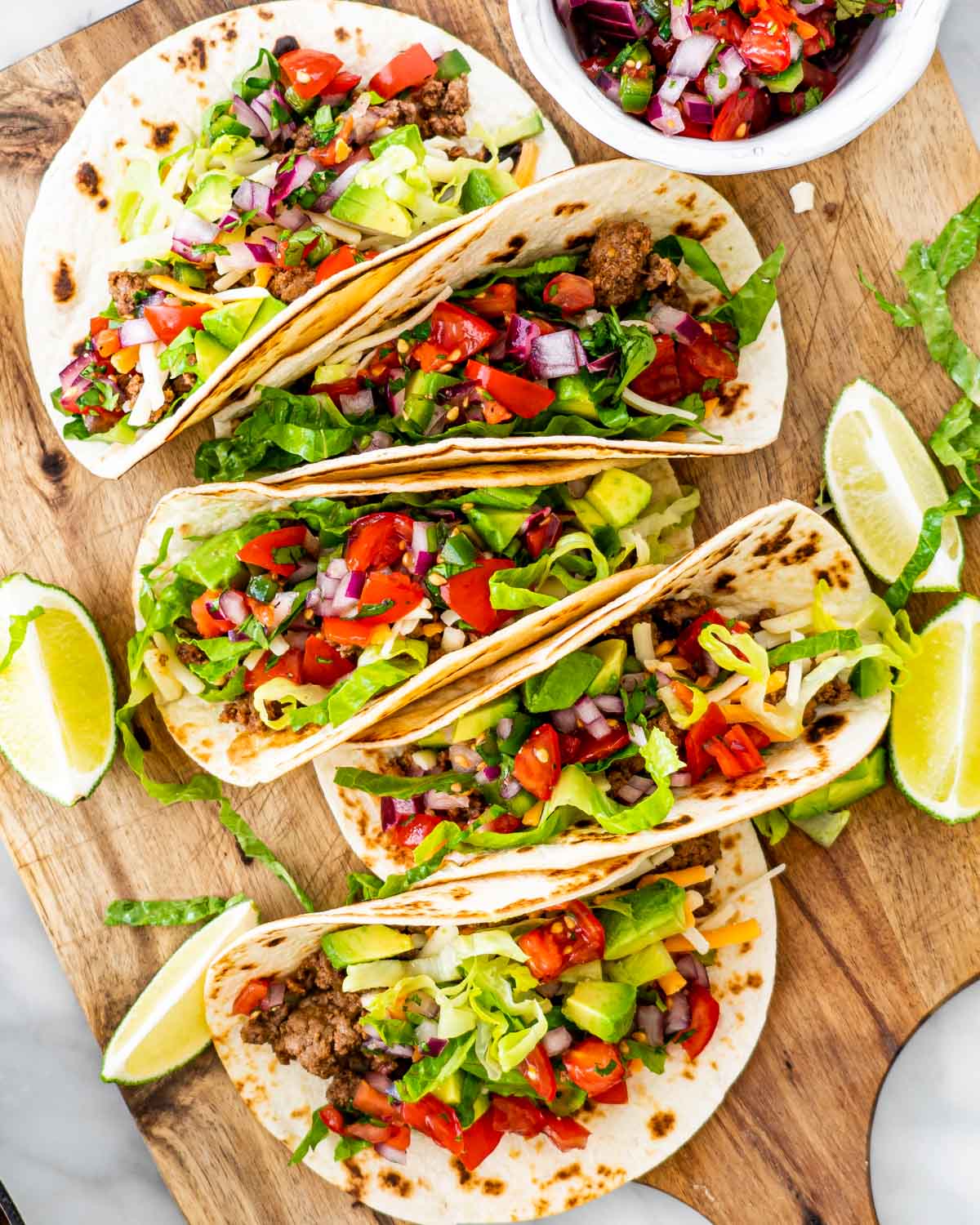 overhead shot of ground beef tacos topped with pico de gallo on a cutting board