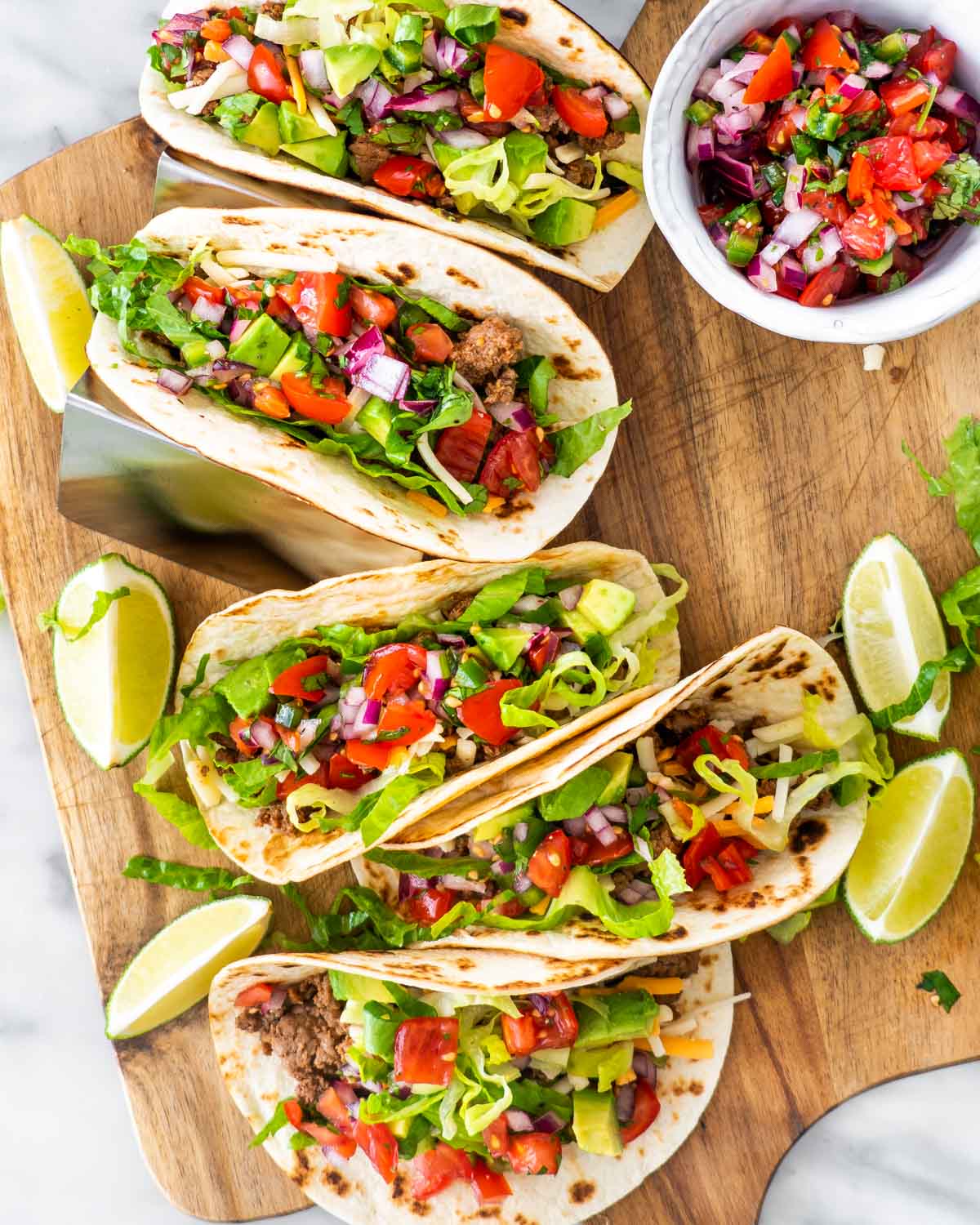 overhead shot of ground beef tacos topped with pico de gallo on a cutting board