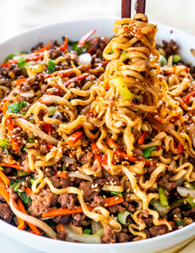 sideview shot of hoisin beef noodles in a white bowl with chop sticks twirling some noodles