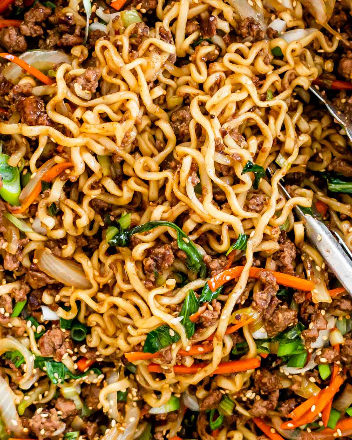 closeup overhead shot of hoisin beef noodles in a wok with a pair of tongs in it