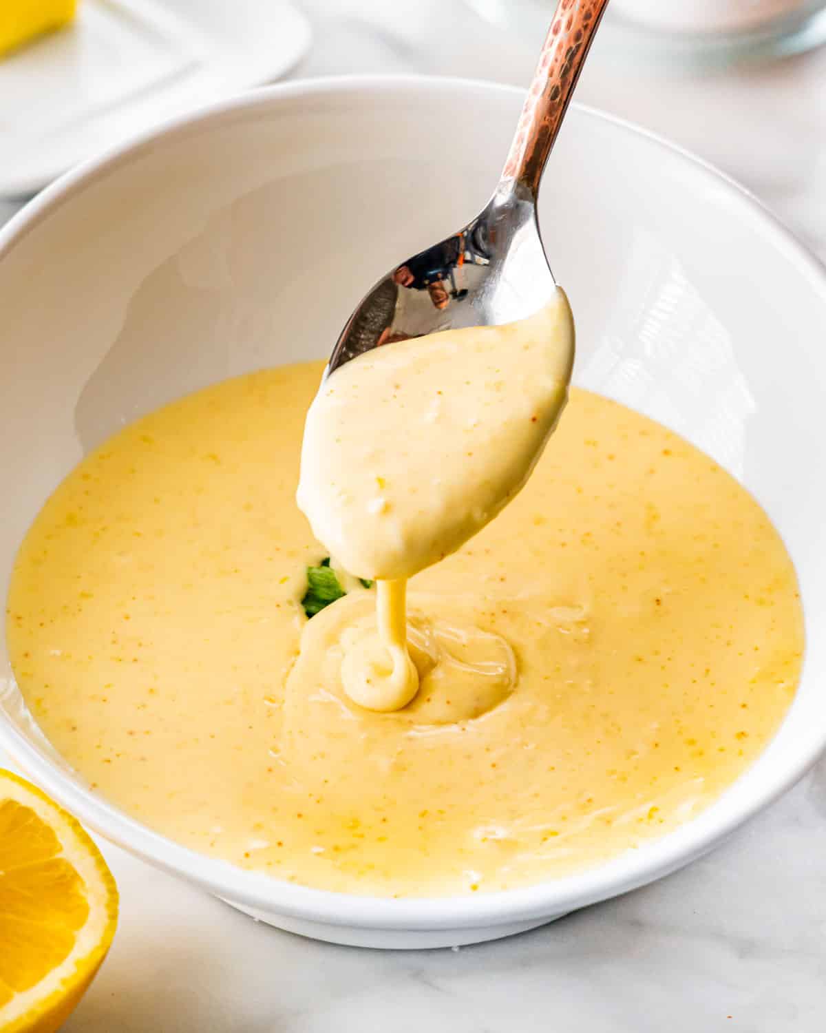 a spoon spooning some hollandaise sauce from a bowl