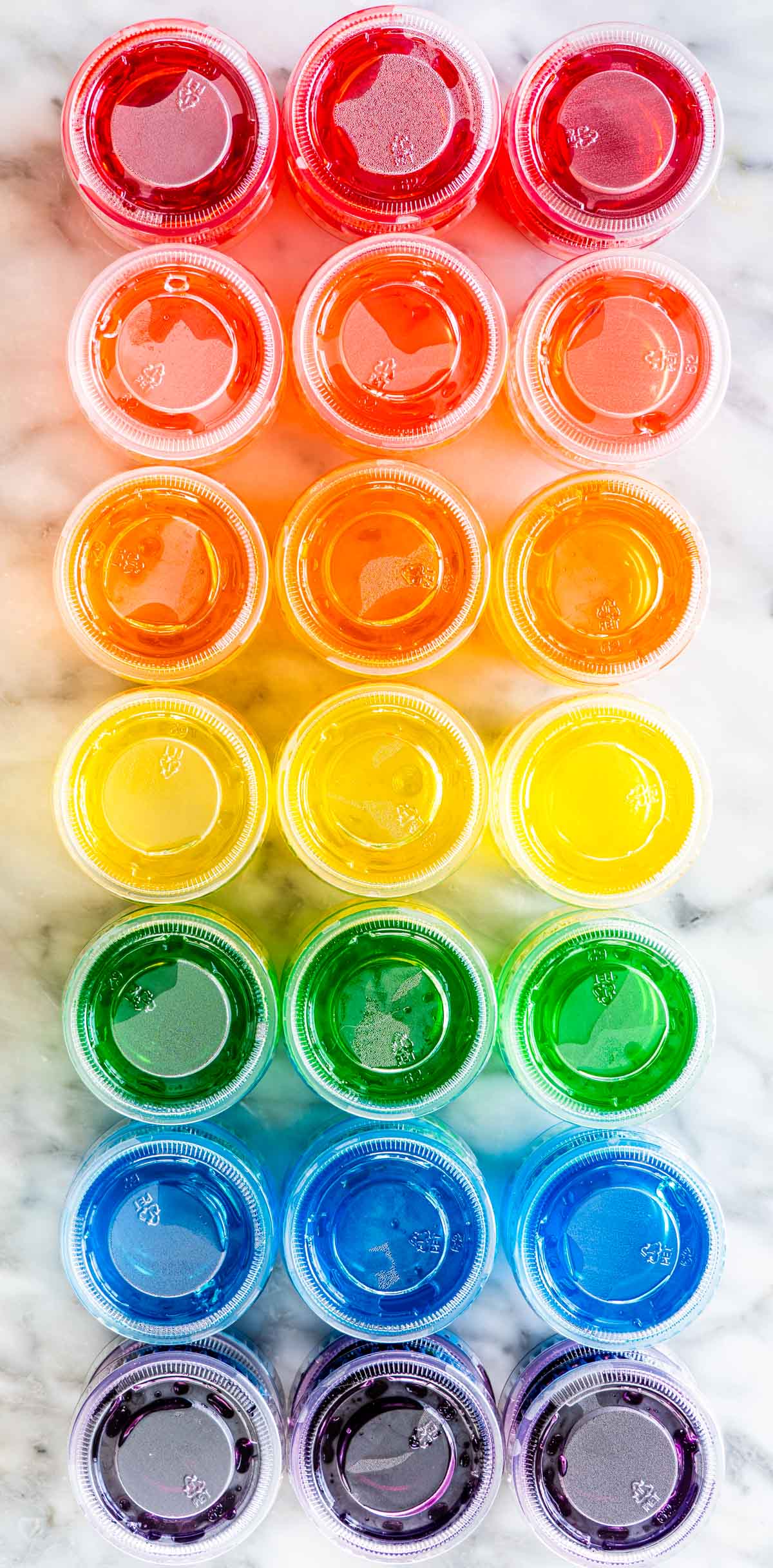 overhead shot of jello shots all different colors in little plastic cups with lids on