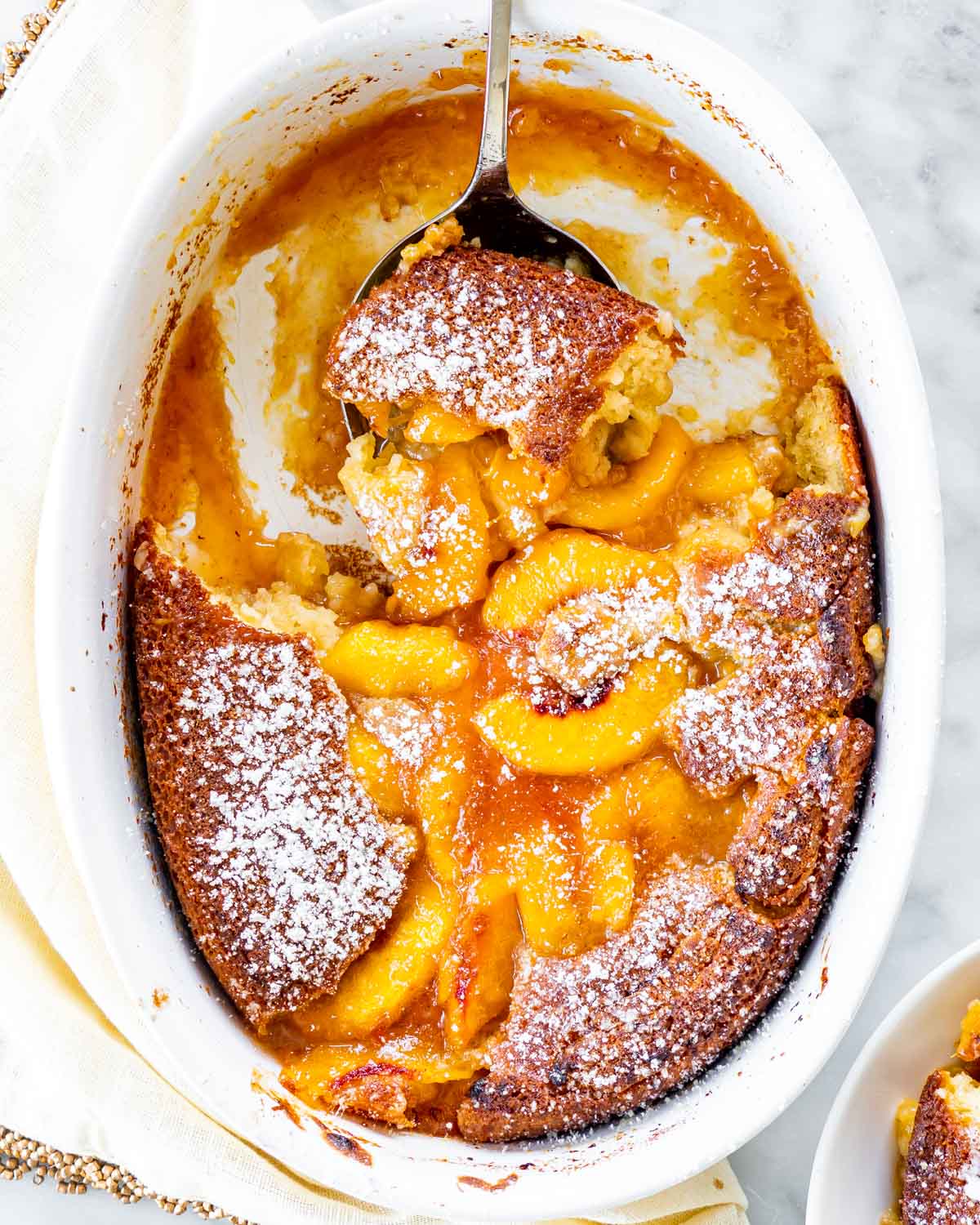 overhead shot of freshly baked peach cobbler in a baking dish with a serving spoon holding a piece 