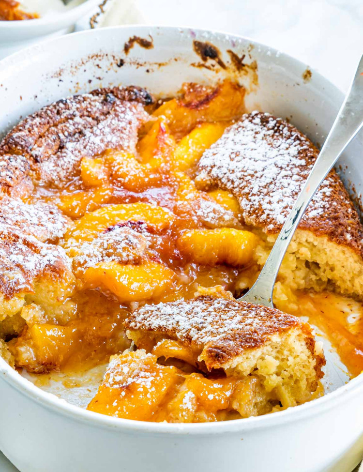 side view shot of freshly baked peach cobbler in a baking dish with a serving spoon holding a piece