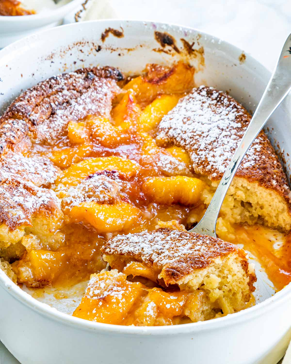 side view shot of freshly baked peach cobbler in a baking dish with a serving spoon holding a piece 