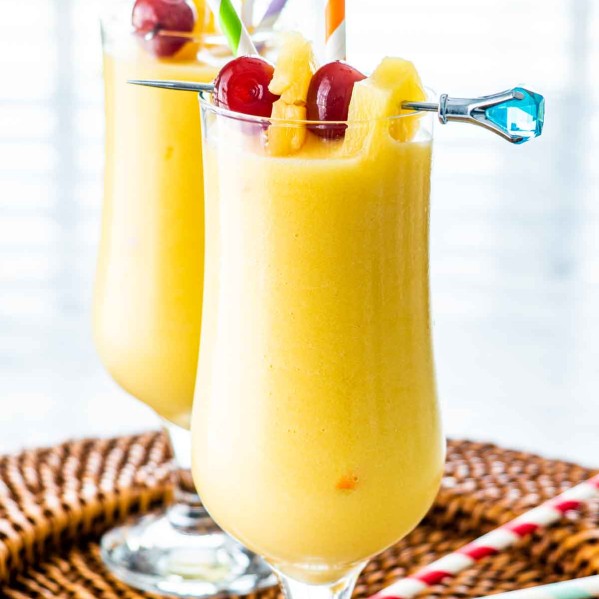 two glasses with Piña Colada and garnished with maraschino cherries and pineapple wedges