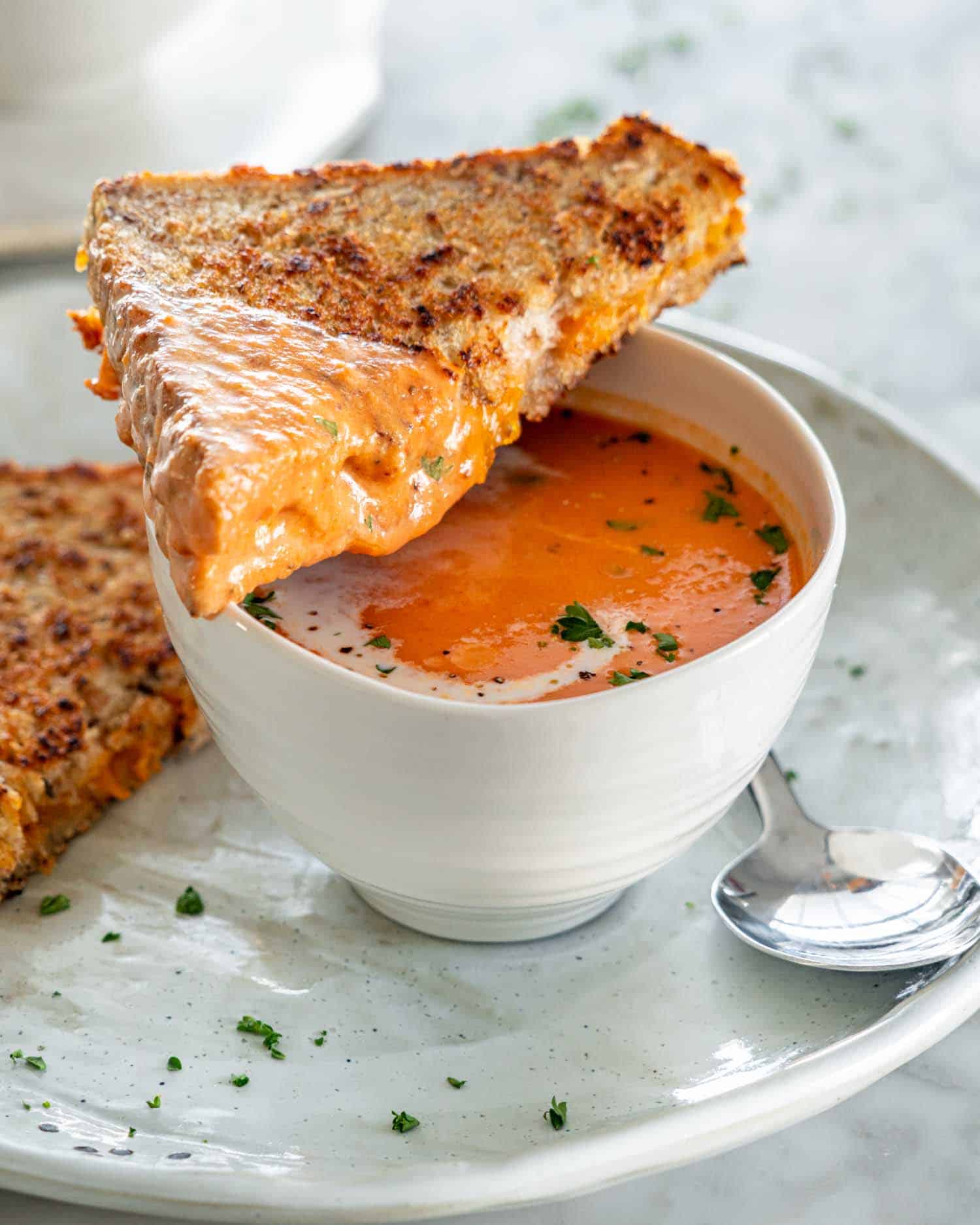 side view shot of tomato bisque in a soup bowl with a half a grilled cheese resting on the bowl