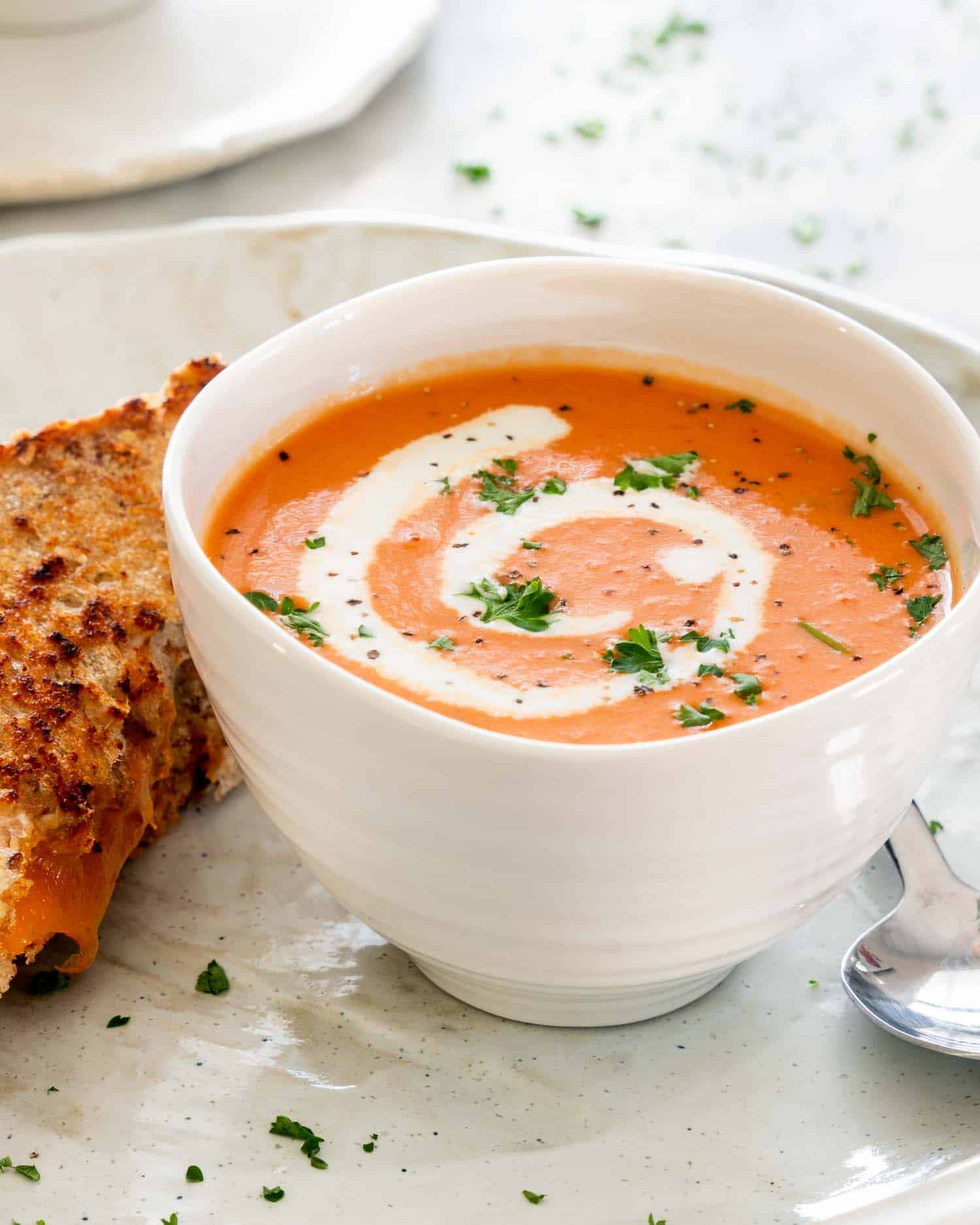 side view shot of tomato bisque in a soup bowl with a grilled cheese sandwich