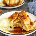 Two plates of apple dumplings drizzled with syrup, served alongside scoops of vanilla and caramel ice cream with a fork.
