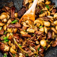 beef mushroom stir fry in a wok with a wooden spoon in it