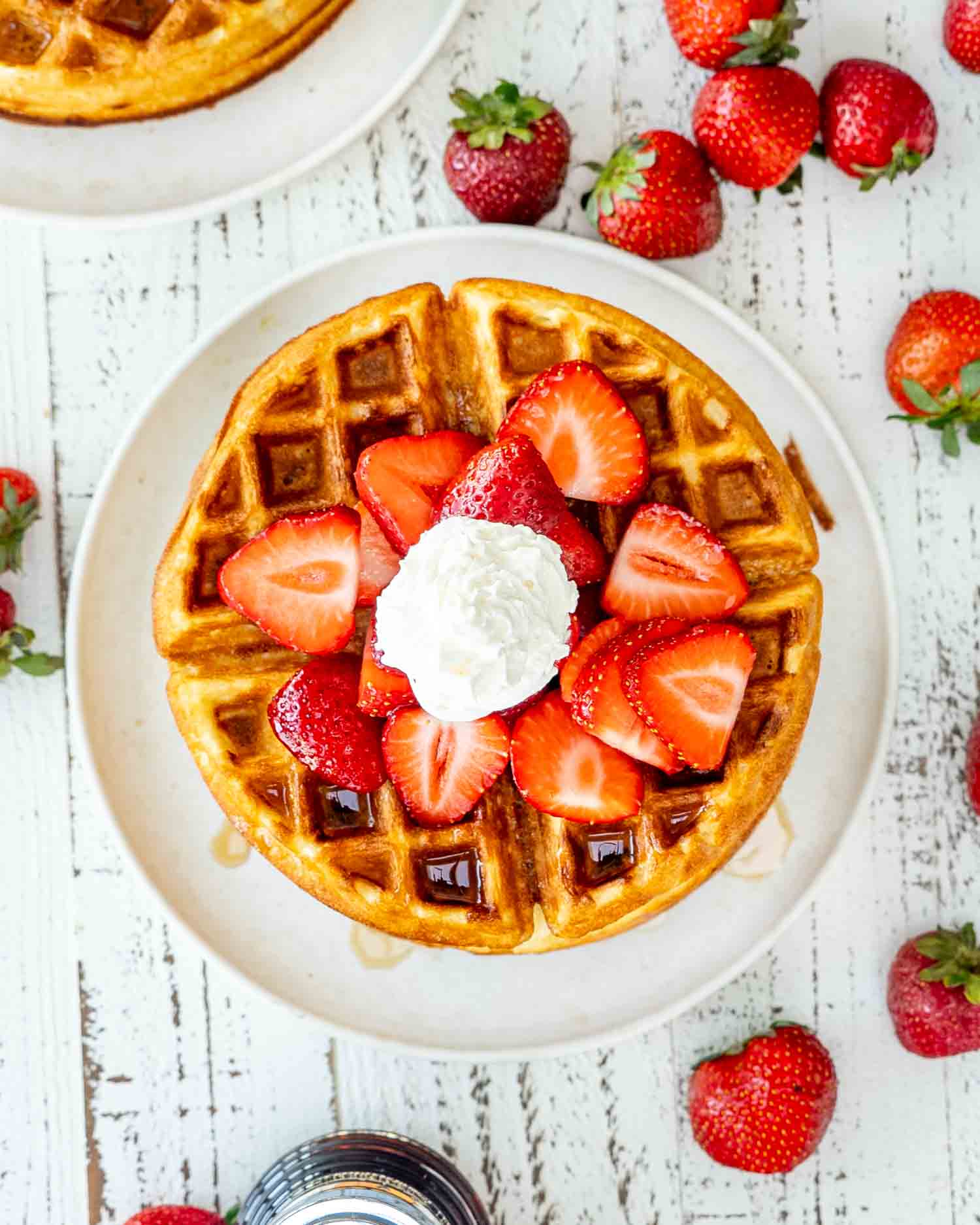 a stack of belgian waffles on a white plate topped with maple syrup, strawberries and whipped cream