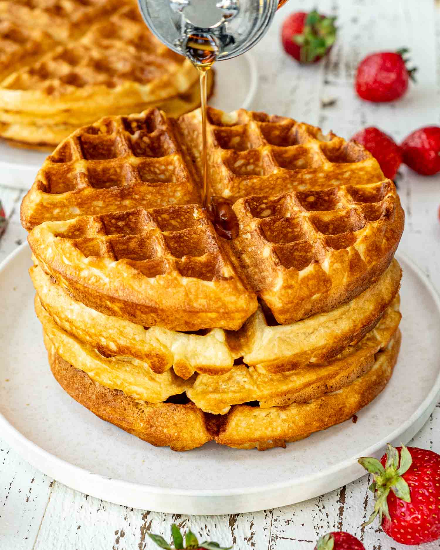 a stack of belgian waffles on a white plate topped with maple syrup.