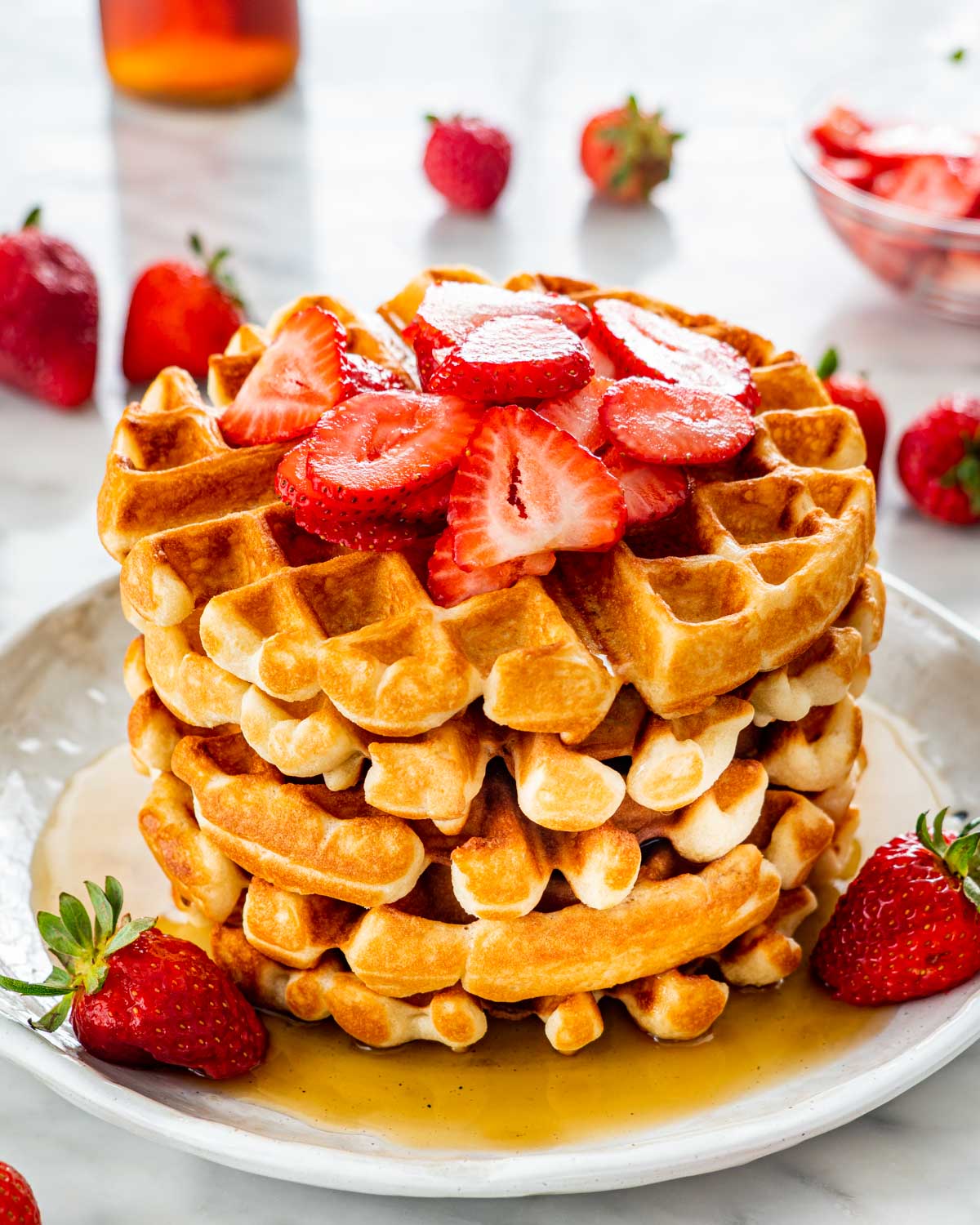 a stack of belgian waffles on a white plate topped with maple syrup, strawberries