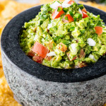 a stone bowl filled with freshly made guacamole surrounded by tortilla chips