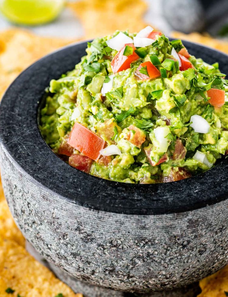 a stone bowl filled with freshly made guacamole surrounded by tortilla chips