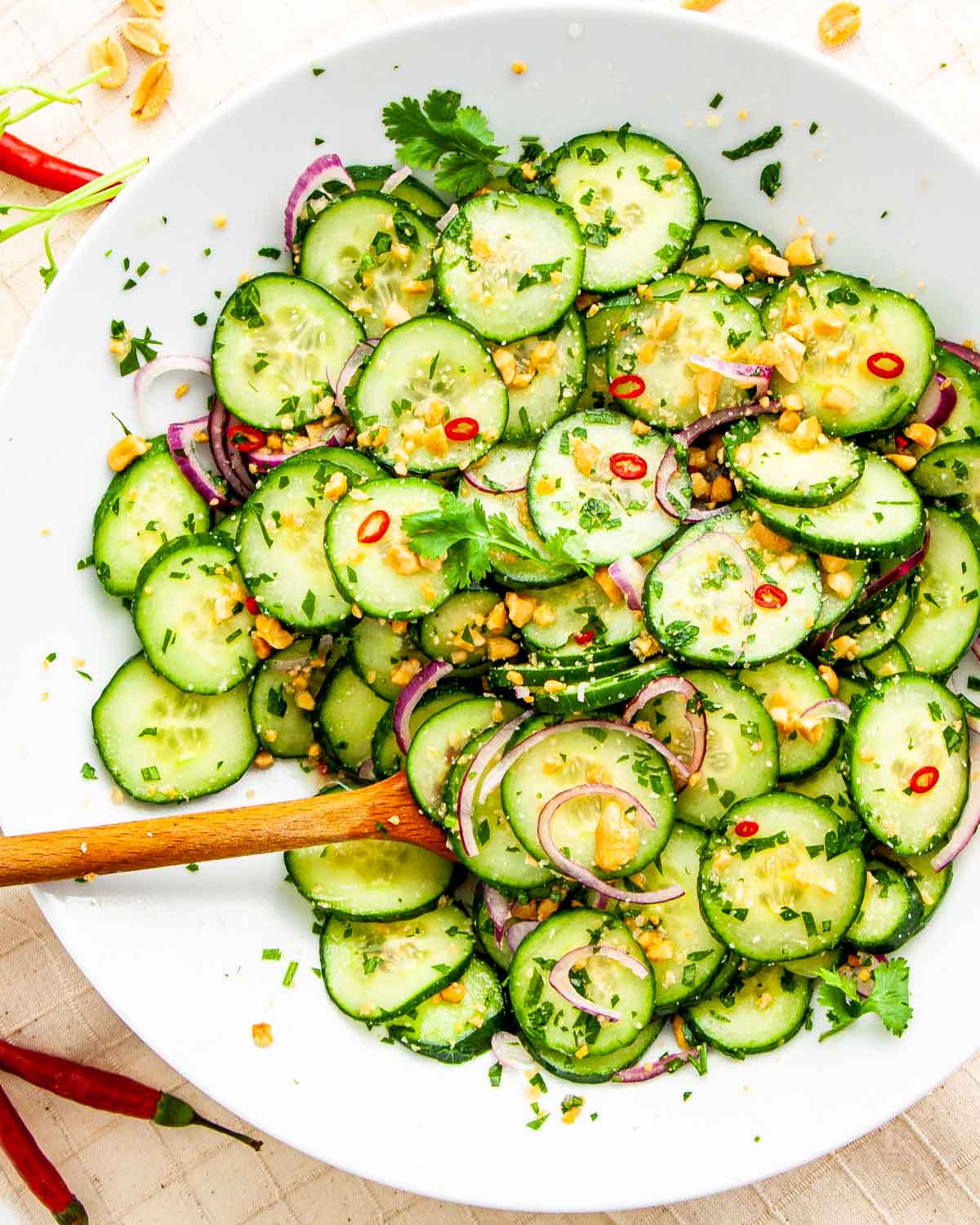 overhead shot of thai cucumber salad freshly made in a white plate with a wooden spoon inside
