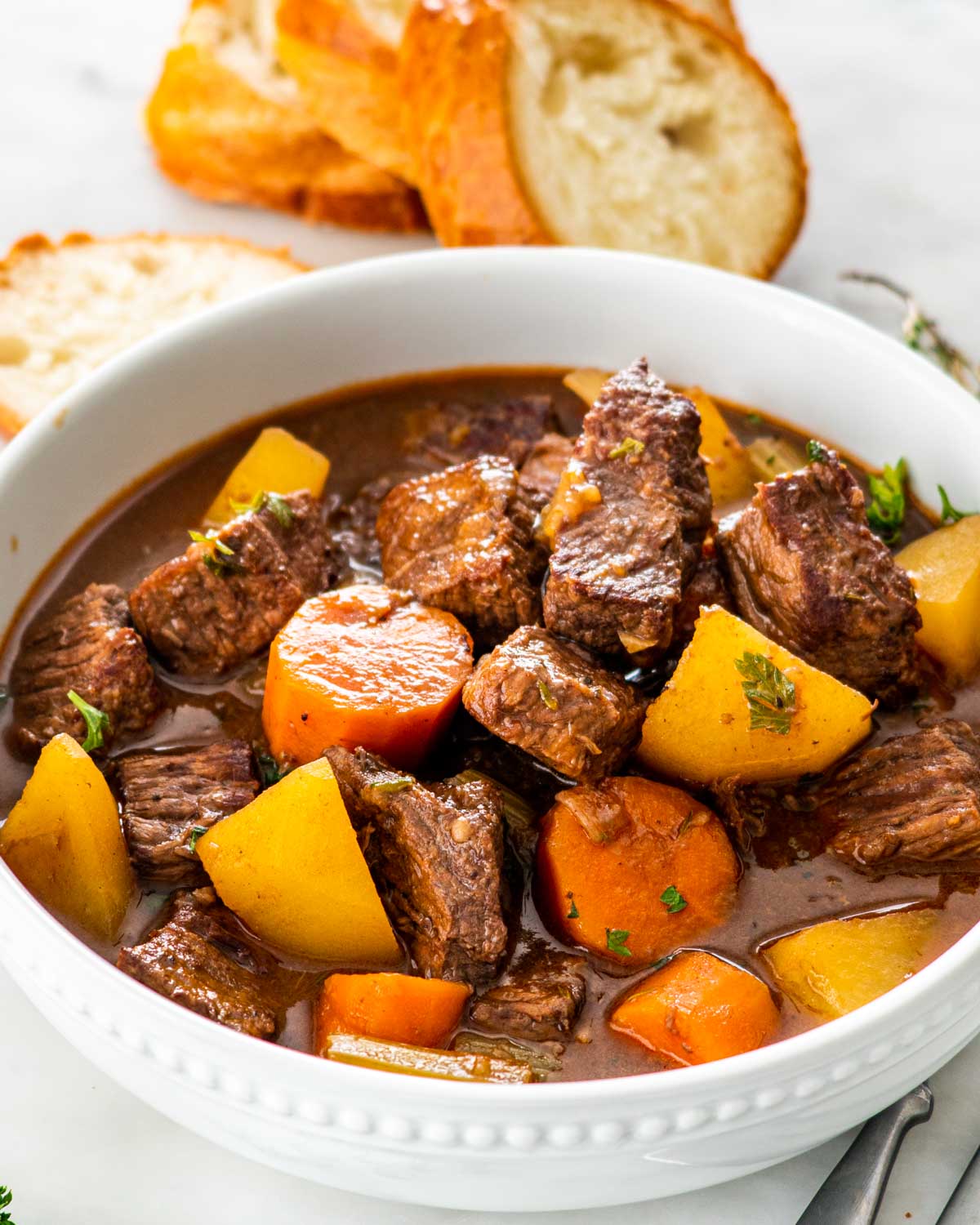 closeup of beef stew in a white bowl with some crusty bread.