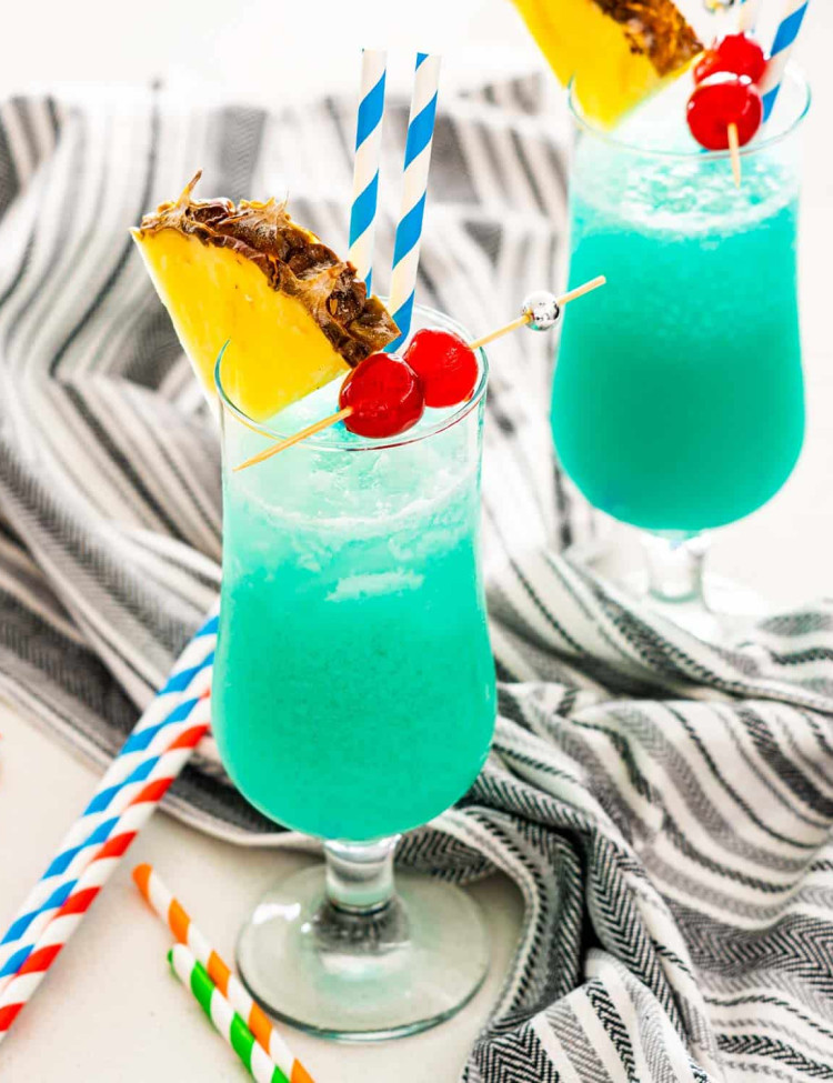two glasses with blue hawaiian garnished with pineapple slice and maraschino cherries.
