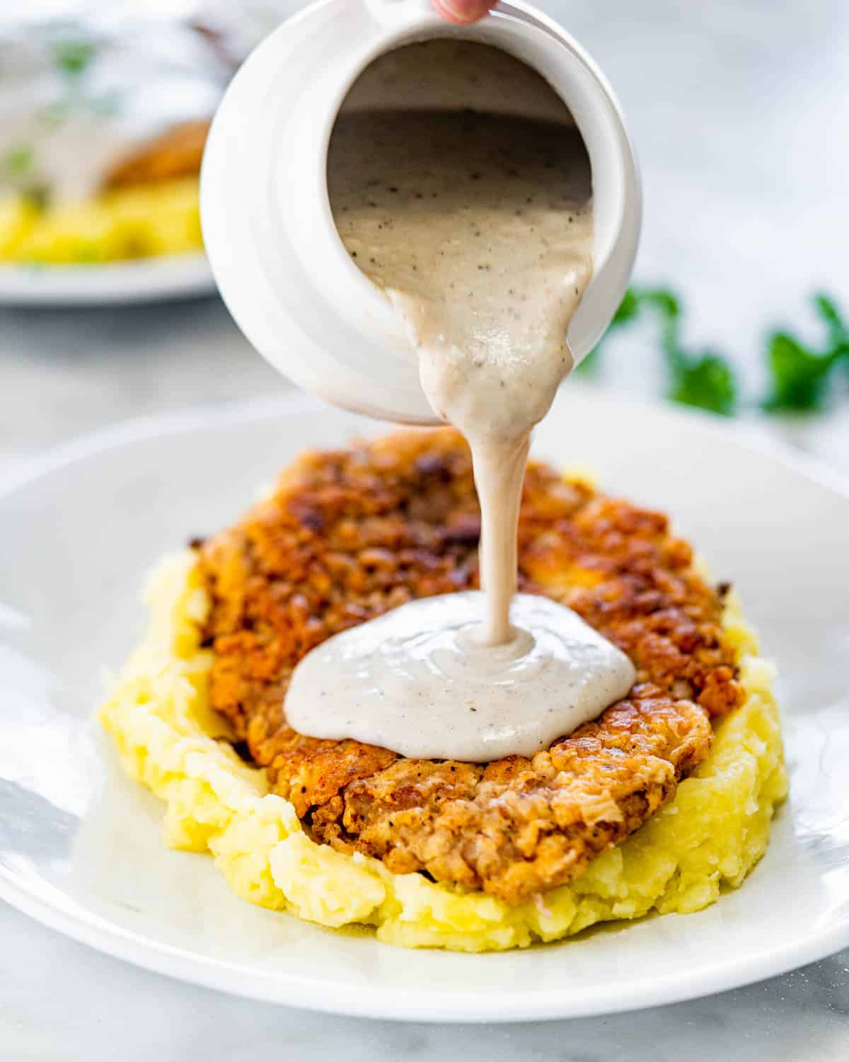 pouring gravy from a jug over a plate with mashed potatoes and chicken fried steak
