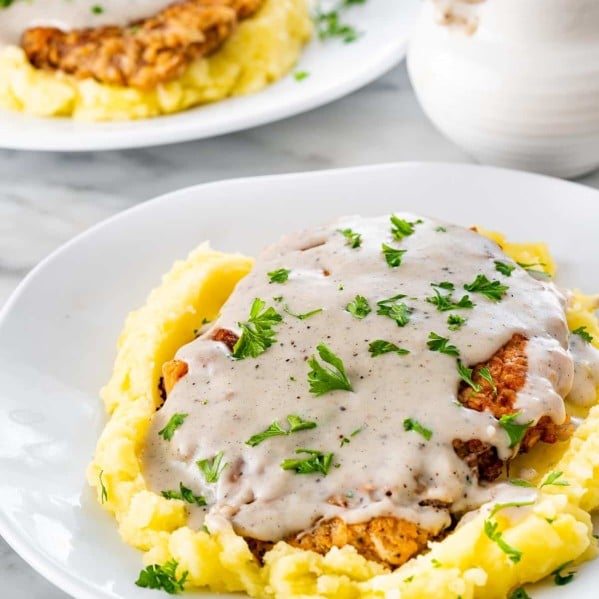 chicken fried steak on a bed of mashed potatoes with gravy on a white plate.
