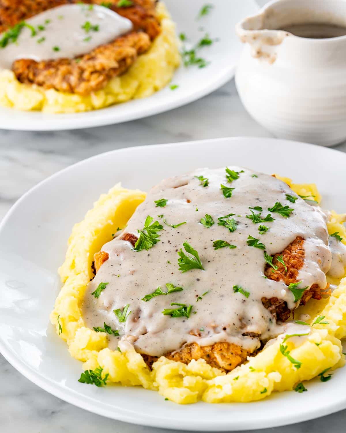 chicken fried steak on a bed of mashed potatoes with gravy on a white plate.