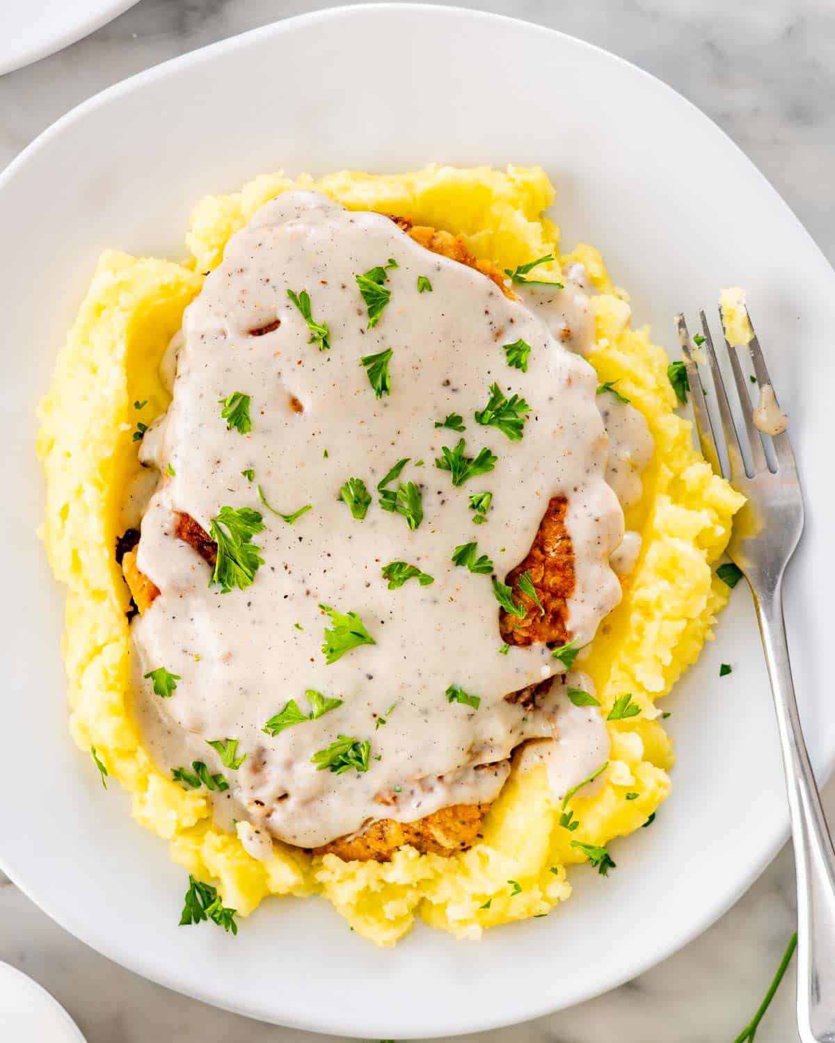 overhead shot of chicken fried steak on a bed of mashed potatoes with gravy on a white plate.