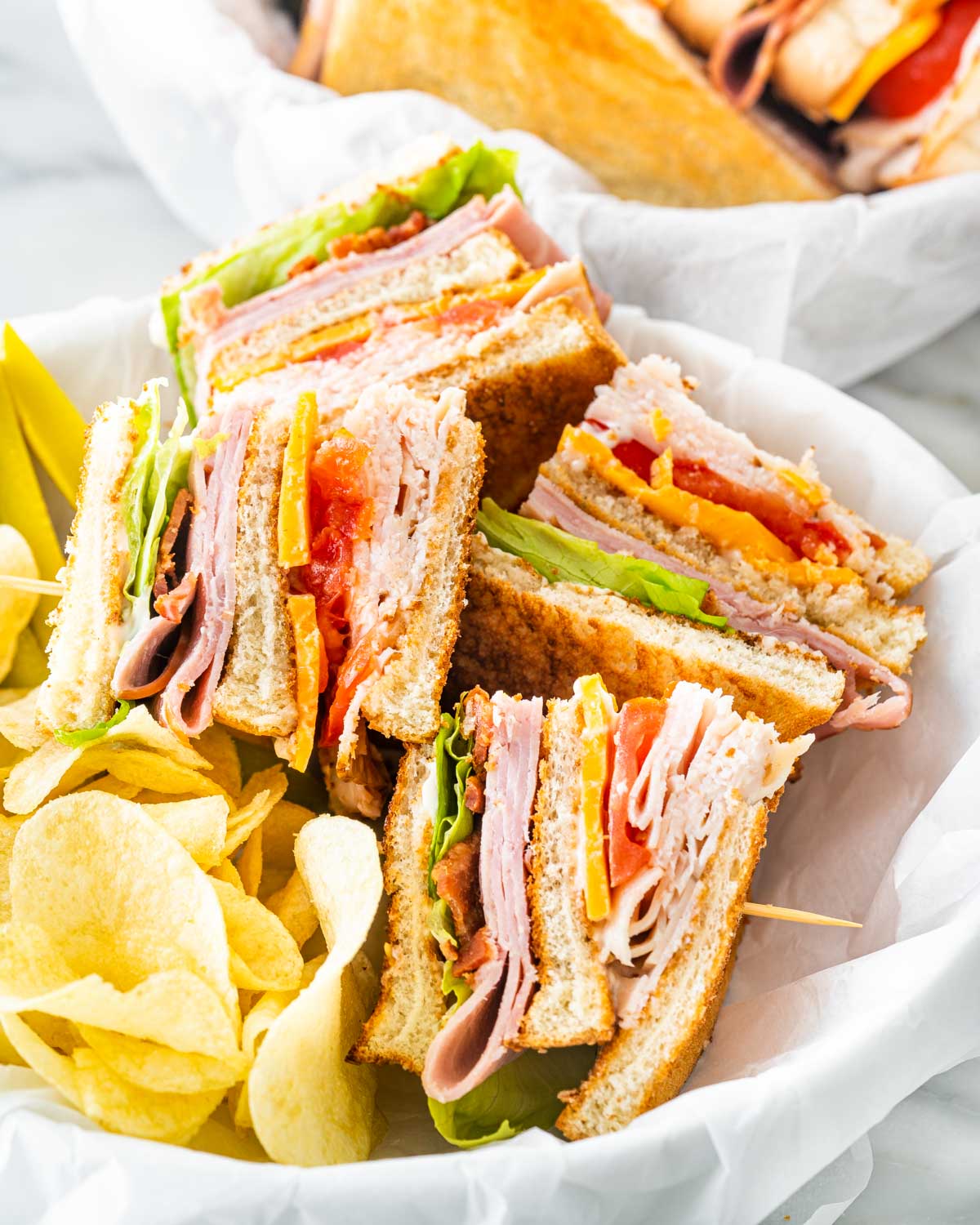 club sandwich cut in quarters with a side of chips and pickles in a basket.