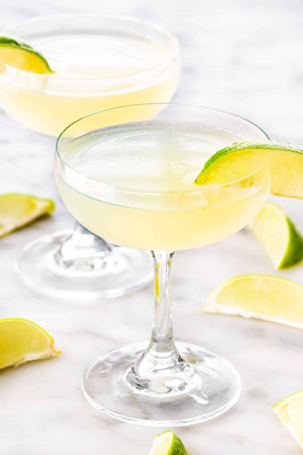 two glasses with daiquiri and garnished with lime wedges.