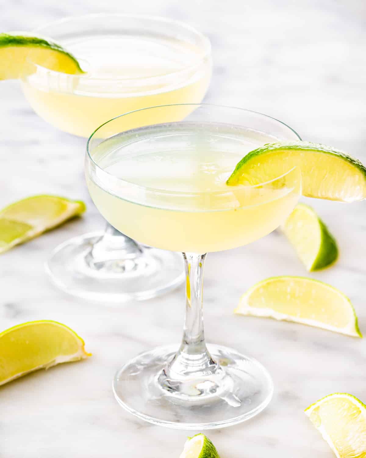 two glasses with daiquiri and garnished with lime wedges.