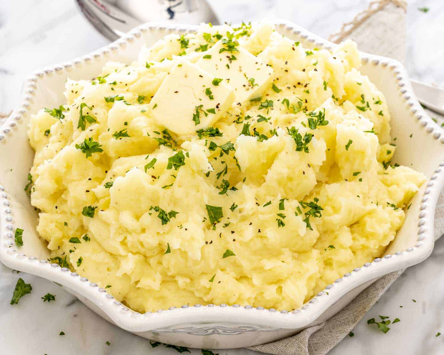 Creamy mashed potatoes made in the Instant Pot, piled high in a decorative bowl and finished with butter and chopped parsley.